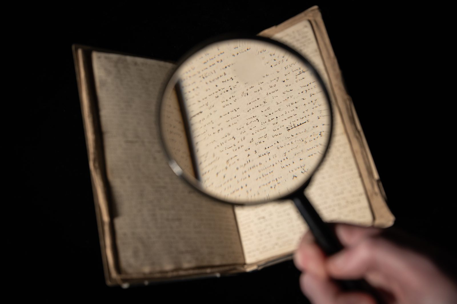 A curator holds a magnifying glass over Charlotte Brontë’s Fireside Tales, a handwritten manuscript