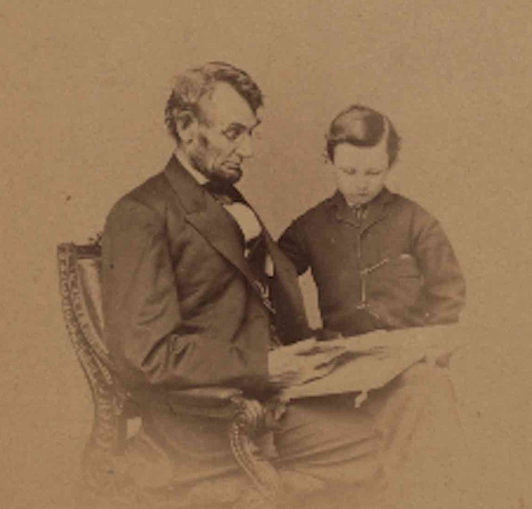 Original portrait photograph of Lincoln seated with a book and his son Tad, taken February 9, 1864
